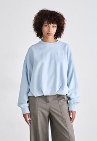 Lyseblå oversized sweatshirt i mykt stoff med rund hals og ribbestrikkede mansjetter, kombinert med grå høyhviste vide bukser.