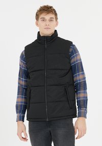 Schwarze gepolsterte Weste mit hohem Kragen, die zwei seitliche Reißverschlusstaschen und eine glatte Textur aufweist, über einem blauen karierten Langarmhemd.