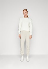 Hvit teksturert genser med ribbede mansjetter, sammen med lyse beige joggers og hvite sneakers, som skaper et avslappet, uformelt utseende.