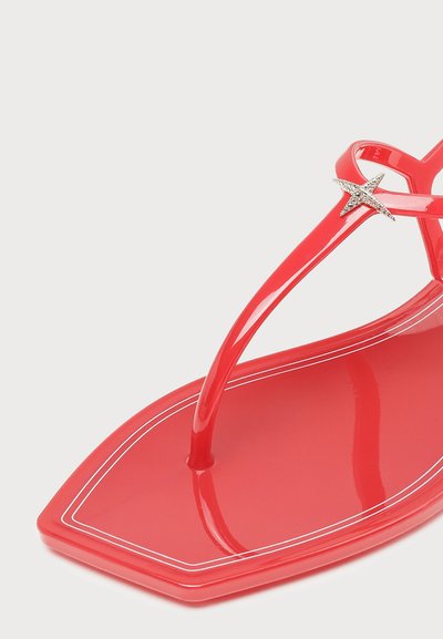 Κόκκινο γυαλιστερό σαγιονάρι με μυτερή μύτη, λευκό διπλό περίγραμμα και μικρή ασημένια διακόσμηση αστερία στο λουράκι.