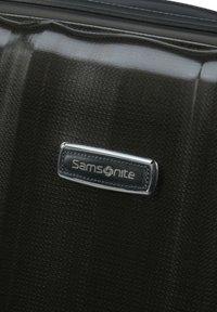 Black suitcase with textured surface, featuring a silver Samsonite logo on a black leather patch, and a glossy finish.