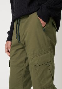Olijfgroene cargo pants gemaakt van duurzaam materiaal, met meerdere grote zakken, een verstelbare trekkoord taille en een gestructureerde afwerking.
