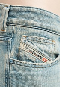 Τσέπη από ανοιχτόχρωμο τζιν με ετικέτα Diesel Industry μερικώς τοποθετημένη μέσα, με ξεθωριασμένο ύφασμα και εμφανείς λεπτομέρειες ραφής.