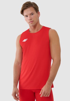 Młody mężczyzna w czerwonej bezrękawnikowej koszulce sportowej z białym logo 4F na piersi, stojący na jednolitym jasnym tle.