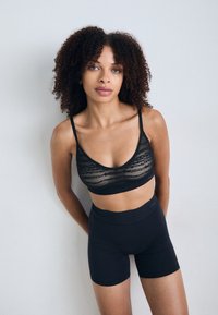 Crni čipkasti bralette s tankim trakama i crnim šortsevima visokog struka, s glatkom teksturom i minimalnim dizajnom.