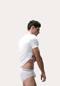 T-shirt bianco in cotone abbinato a slip bianchi con vita nera "AUTOGRAPH", mostrato su una persona vista di lato.