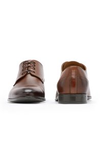 Scarpe da cerimonia in pelle marrone con finitura liscia, dotate di un design con lacci e suola robusta. Include dettagli di cucitura sottili.
