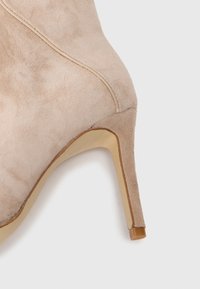 Bottine en daim beige avec un talon effilé, des détails de coutures proéminents et une finition lisse et discrète.