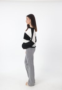 Maglione a righe bianche e nere con vestibilità ampia e scollo rotondo, abbinato a jeans a zampa d'elefante grigi chiari a vita alta. Sandali bassi.