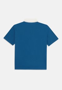 Plava polo majica s bijelim ovratnikom, kratkim rukavima i glatkom teksturom. Ima jednobojnu boju bez vidljivih uzoraka ili logotipa.