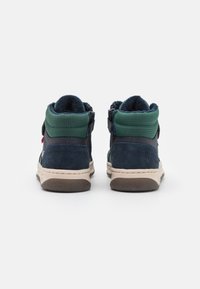 Las zapatillas altas presentan un upper de ante azul marino y malla verde, cierre de cremallera en el lateral y una suela de goma color crema. Forro de felpa acogedor visible.