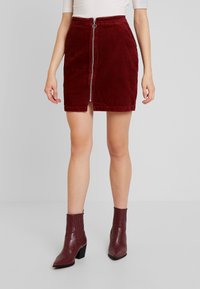 Burgunderfärgad kordkjol med dragkedja framtill och midjeband. Kombinerad med texturerade burgunderfärgade ankelstövlar med klack.