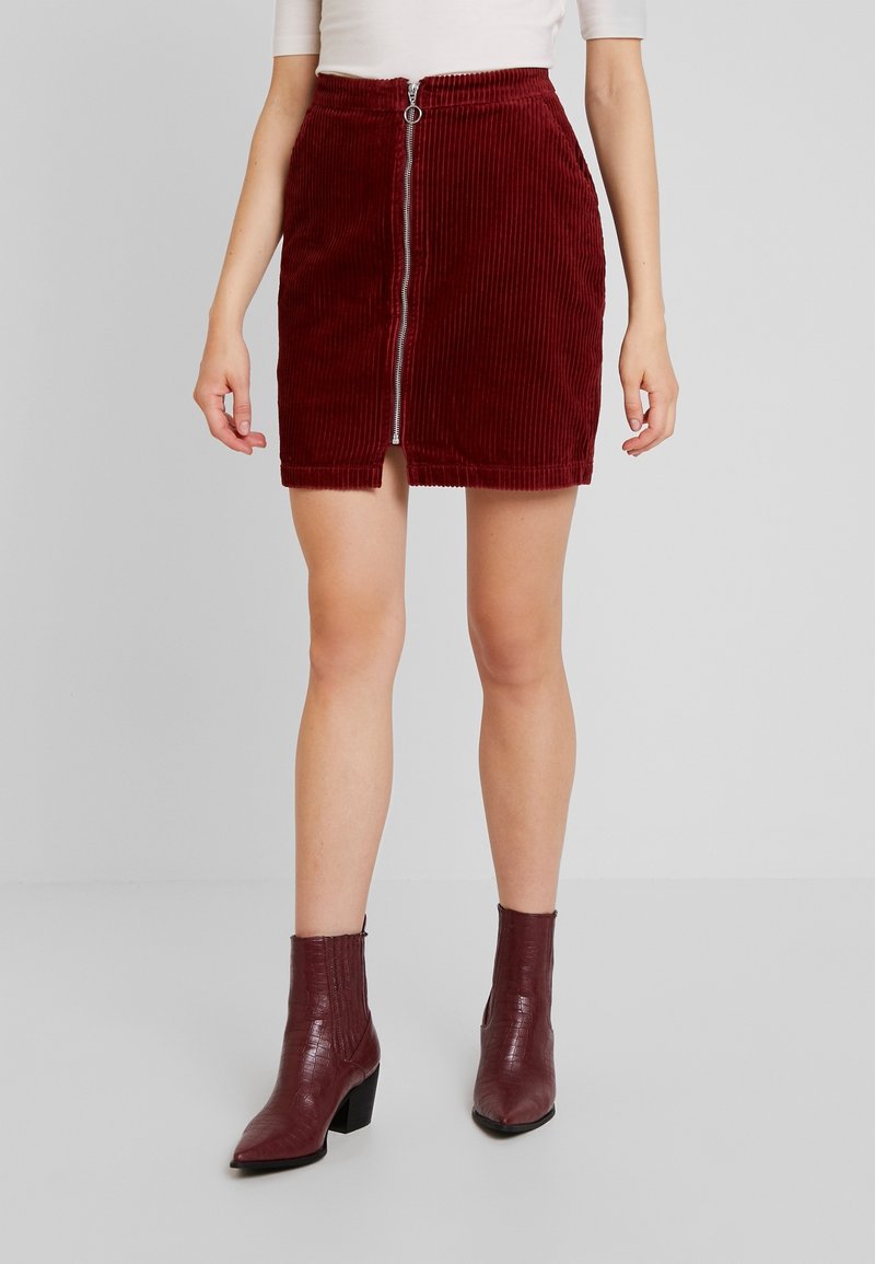 Burgunderfärgad kordkjol med dragkedja framtill och midjeband. Kombinerad med texturerade burgunderfärgade ankelstövlar med klack.