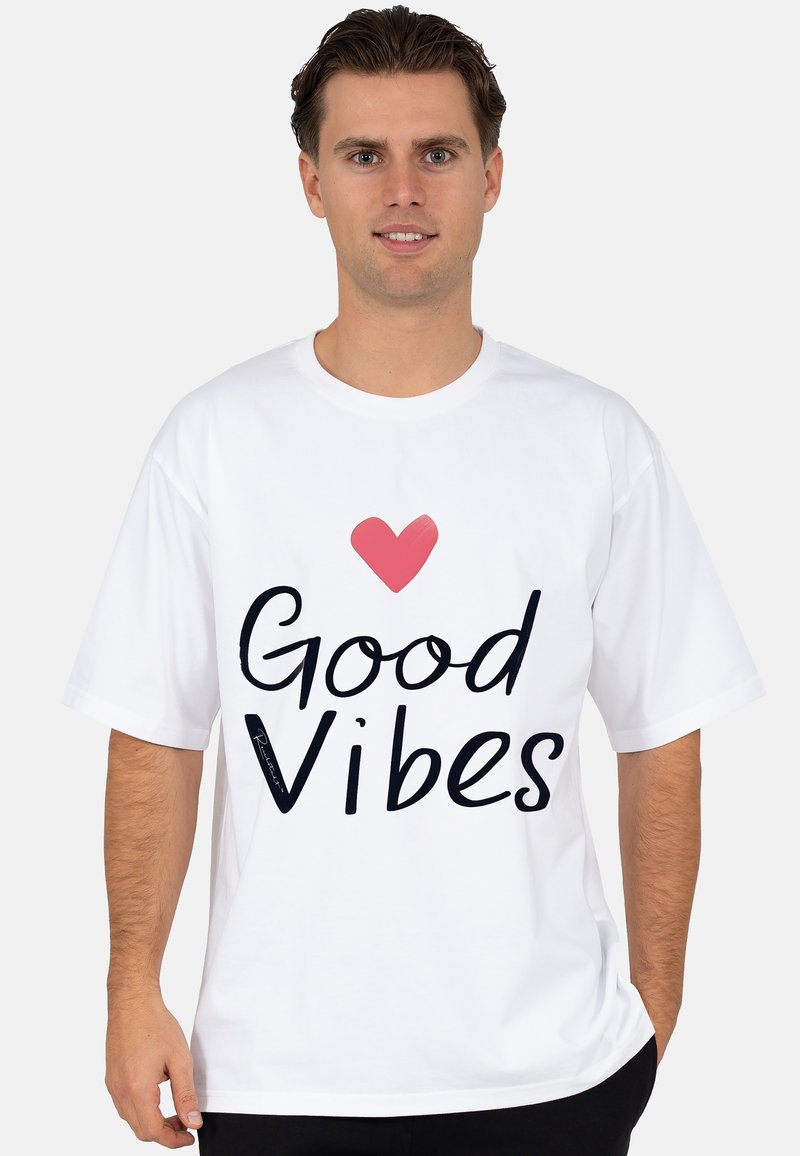 Witte katoenen t-shirt met de tekst "Good Vibes" in het zwart en een roze hartaccent. Korte mouwen, relaxte pasvorm, gladde textuur.
