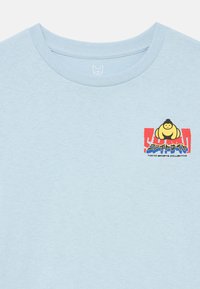 Svetlomodré bavlnené tričko s okrúhlym výstrihom. Na tričku je grafický dizajn v červenej, žltej a modrej farbe so sumo postavičkou a japonským textom.