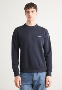 Sudadera azul marino en mezcla de algodón, con cuello redondo acanalado, mangas largas y un pequeño logotipo bordado en el pecho.