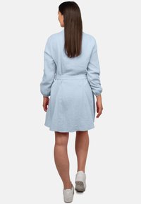 Abito azzurro chiaro, texture, con maniche lunghe, svasato in vita con una cintura coordinata. La gonna si allarga leggermente all'orlo. Indossati sneakers bianche.