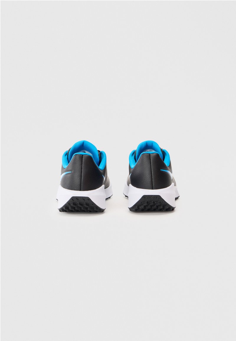 Un paio di scarpe da ginnastica nere con rivestimento interno blu e suole bianche, viste da dietro su uno sfondo grigio chiaro uniforme.