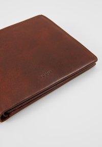 Bruine leren portemonnee met een gladde textuur, voorzien van subtiele logo-embossing en nette stiksels langs de randen.
