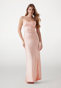 Abito da sera di satin rosa con spalline sottili, silhouette aderente, spacco laterale e texture liscia. La lunghezza arriva fino alle caviglie.