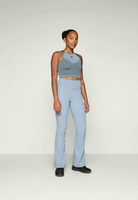 Lyseblå atletisk crop top med ribbet tekstur og flagrende matchende bukser; begge laget av elastisk stoff, sammen med svarte fottøy.