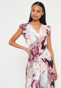 Kleita ar ziedu rakstu, bārkstainām kapu piedurknēm, V-veida izgriezumu un plūstošu siluetu. Krāsas: rozā, violeta un krēmkrāsa uz fakturētas auduma.