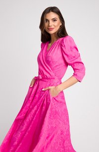 Różowa sukienka kopertowa z bufiastymi rękawami, z paskiem, kieszeniami bocznymi i kwiatowym wzorem wytłoczonym na materiale.