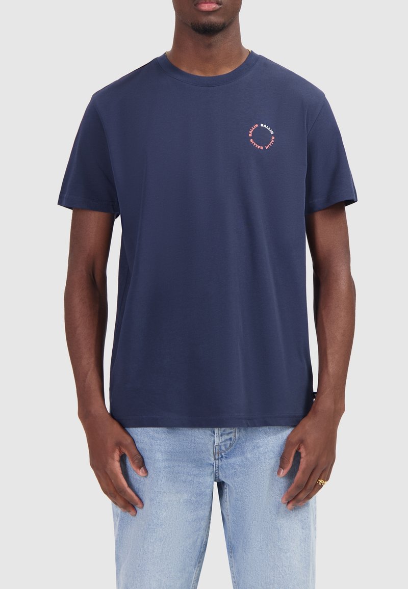 Donkerblauwe katoenen t-shirt met ronde hals, korte mouwen en een kleine cirkelvormige grafiek op de linkerborst in rood en wit.