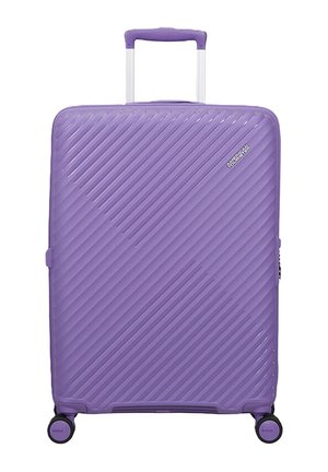 Valigia rigida viola con scanalature diagonali, quattro ruote girevoli, manico telescopico e logo American Tourister sulla parte anteriore.