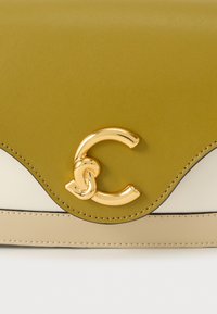 Handtas van olijfgroen leer met goudkleurige accenten, met een kenmerkend gebogen ontwerp en crèmekleurige details.