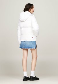 Giacca imbottita bianca con cappuccio, con un design corto e cuciture visibili. Abbinata a una gonna di jeans e scarpe nere.
