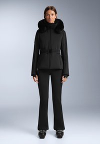 Fekete kabát műszőrme gallérral, cipzárral záródik és öves derékkal rendelkezik. Feszes fekete nadrággal és platform cipőkkel viselve.