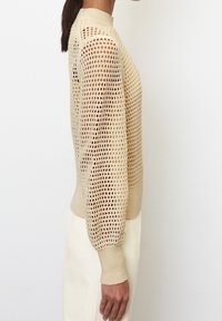 Beżowy sweter dzianinowy z otwartym wzorem siateczkowym, długimi rękawami i żeberkowym okrągłym dekoltem. Gładka faktura z elastycznymi mankietami.