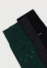 Τρία ζευγάρια κάλτσες: σκούρο πράσινο με πουά, ανθρακί γκρι και μονόχρωμο μαύρο. Όλα έχουν ριμπ ύφανση και το λογότυπο "BOSS".
