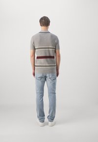 Polo de punto gris con rayas horizontales en rojo y blanco, combinado con jeans azul claro y zapatillas blancas. Diseño simple y ajustado.