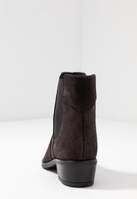 Zwarte suède enkellaars met elastische zijpanelen, lage hak en contrasterende stiksels, met een gladde textuur en een afgeronde neus.