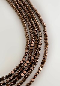 Facettierte Glasperlenkette mit mehreren Strängen in tiefbraunen Farbtönen, die eine glatte Textur und eine reflektierende Oberfläche aufweist, die ihren Glanz verstärkt.