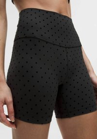 Sorte højtaljede shorts lavet af strækbart stof, der har et prikket mønster og glat tekstur, med detaljeret syning langs sømmen.