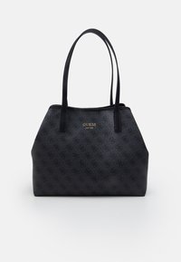 Zwarte Guess schoudertas met monogrampatroon, gouden logo-plaat en twee lange schouderriemen op een witte achtergrond.