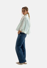 Hvid cropped bluse med en foldet krave og ærme-detajer, parret med lyseblå højtaljede jeans og beige spidse flade sko.