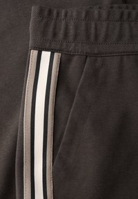 Dunkelgraue Jogginghosen aus strukturiertem Stoff, mit elastischem Bund und seitlicher Tasche, die mit schwarzen, cremefarbenen und beigen Streifen akzentuiert sind.