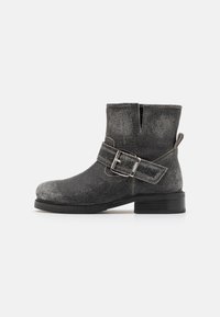 Botas negras hasta el tobillo con un acabado texturizado, detalle de hebilla plateada y tacón apilado. Cuentan con una apertura lateral para facilitar su uso.