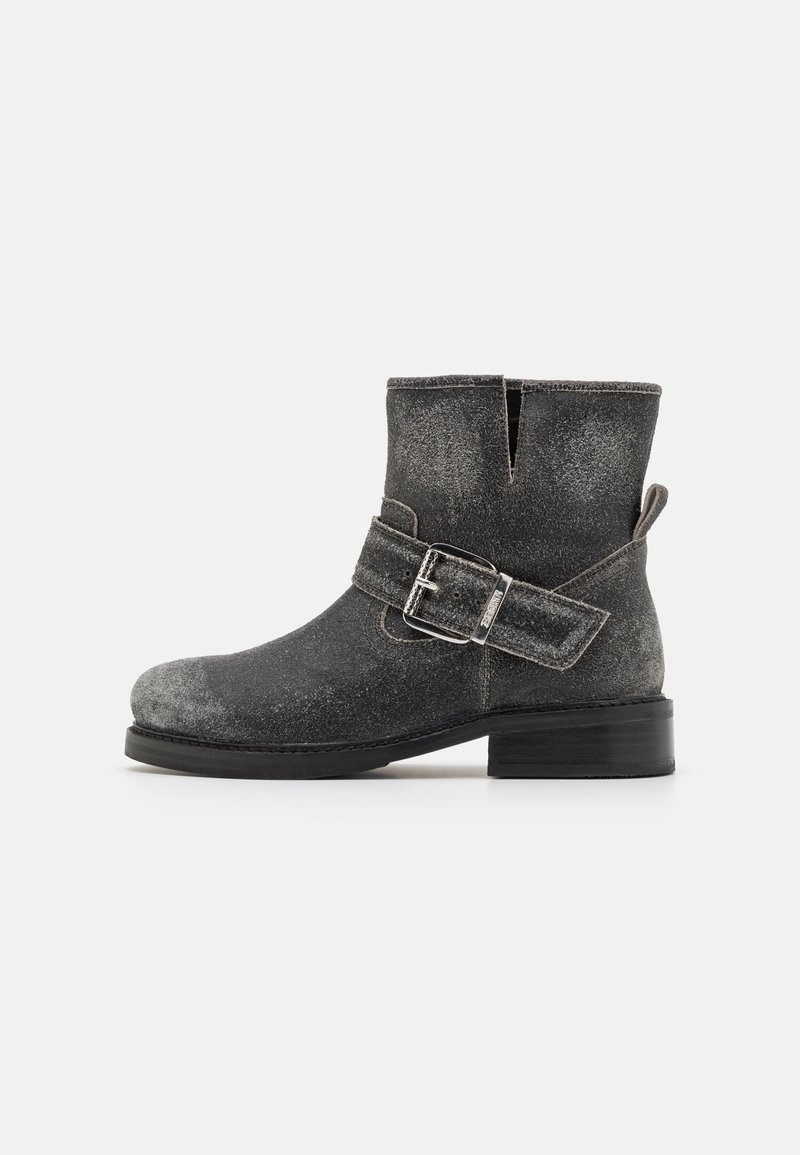 Botas negras hasta el tobillo con un acabado texturizado, detalle de hebilla plateada y tacón apilado. Cuentan con una apertura lateral para facilitar su uso.