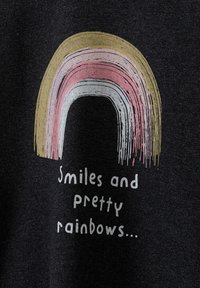 Schwarzes Stoff-T-Shirt mit einem Regenbogen-Graphic in Gold, Rosa und Weiß, darunter der Text "Lächeln und schöne Regenbögen..." in Weiß.