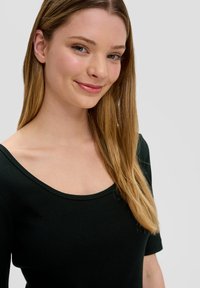 Czarna prążkowana bluzka z szerokim dekoltem i krótkimi rękawami, o gładkiej fakturze i dopasowanym kroju, dopełniona długimi prostymi włosami.