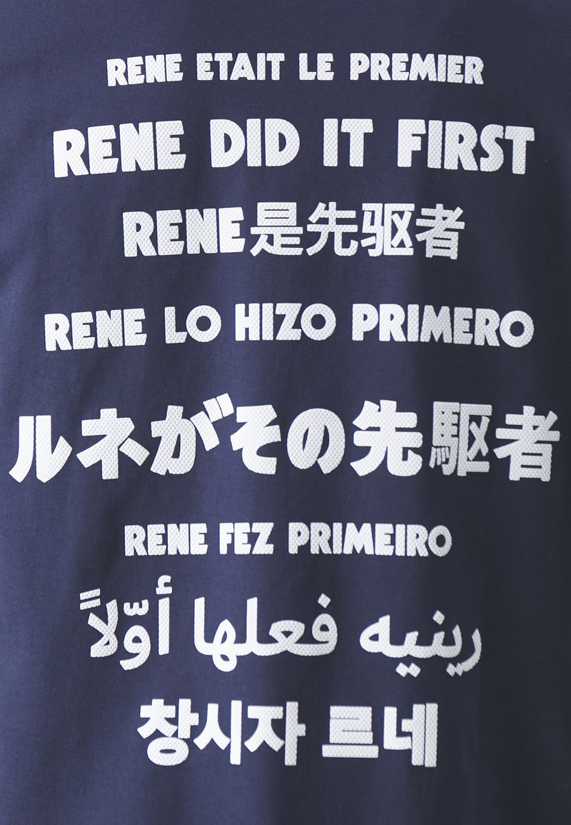 Camiseta azul marino con texto blanco en varios idiomas, mostrando la frase "Rene lo hizo primero" en diferentes tipografías y estilos.