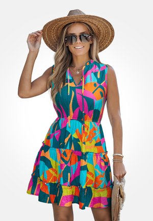 Femme portant un grand chapeau de paille, des lunettes de soleil surdimensionnées, une robe sans manches multicolore à motif abstrait, tenant une pochette beige.
