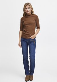 Brown ribbed turtleneck top with short sleeves, paired with blue jeans featuring a zipped pocket and brown ankle boots. Simple, fitted design.