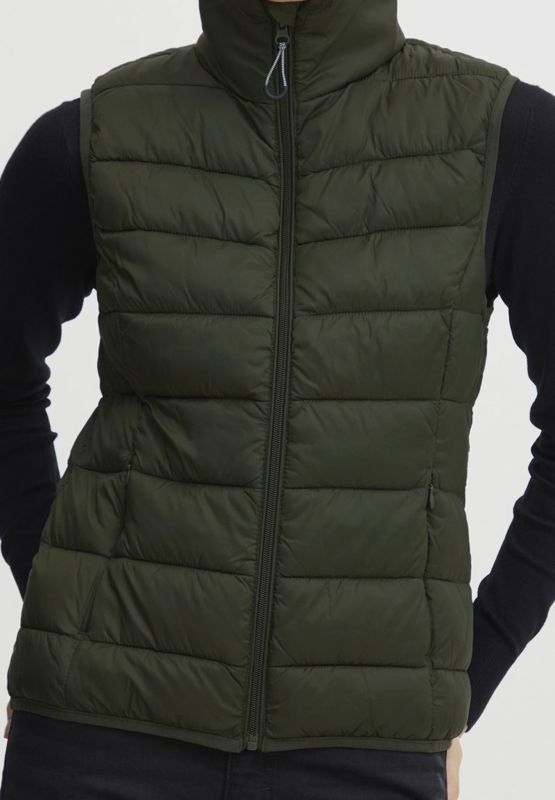 Vadderad väst i mörkgrön färg med hög krage och framdragkedja, med kviltade sektioner och en slät, lätt glänsande yta.