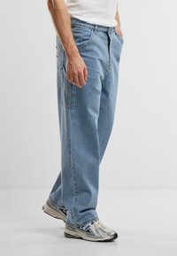 Lys blå denim jeans med løs pasform, forlommer og en baglomme. Båret med sølvfarvede træningssko.